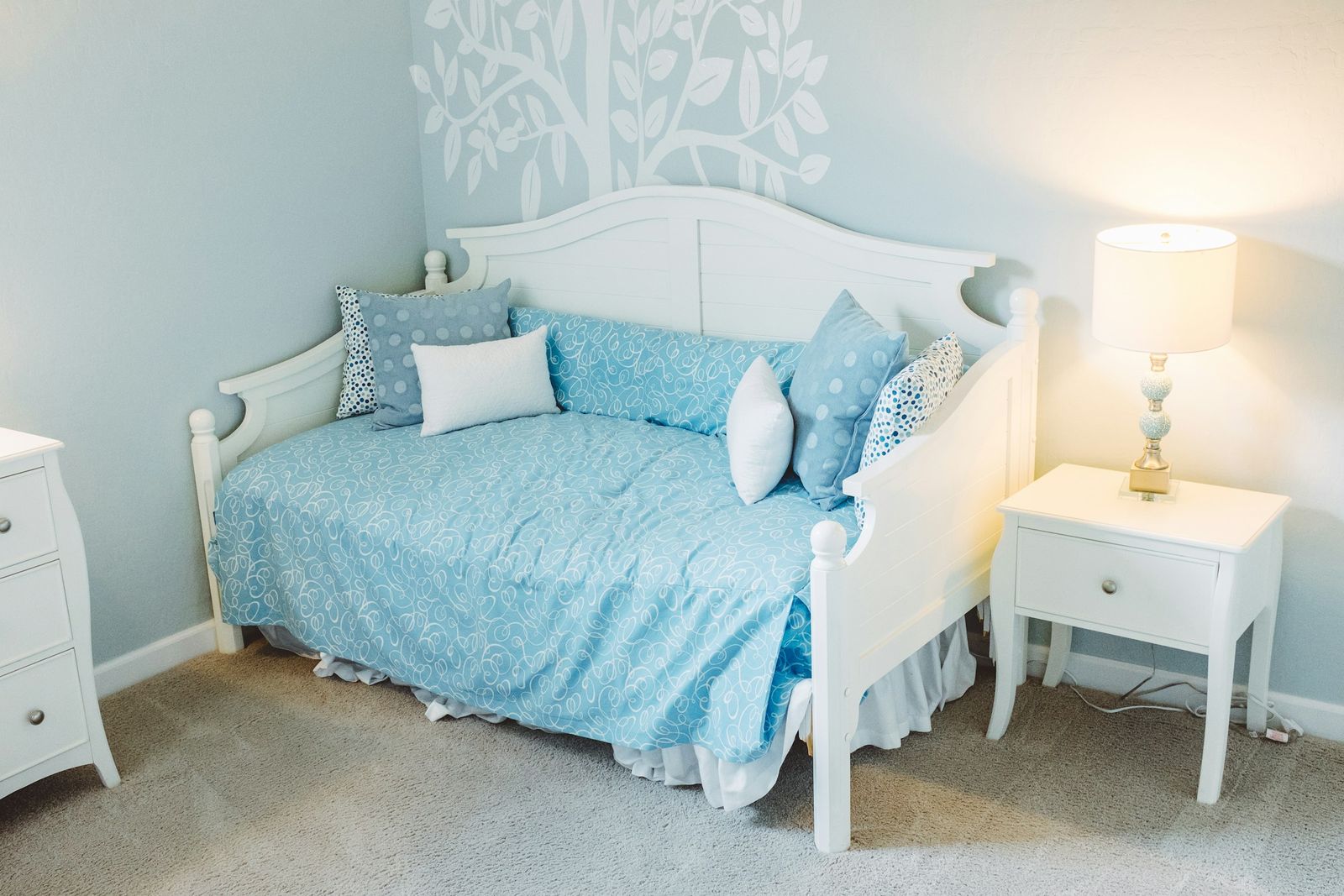 White wooden child's bed with blue bedding and cushions beside a bedside lamp